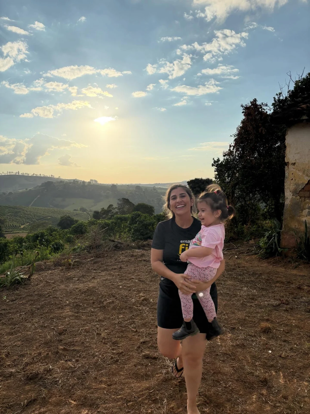 Uma mulher com uma criança diante da paisagem de lavoura ao pôr do sol